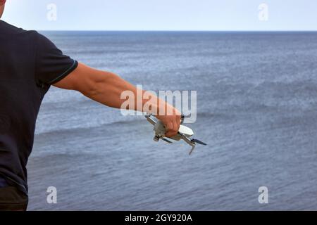 Ein Typ in einem blauen T-Shirt hält einen Quadrocopter in seiner rechten Hand. Der Mann steht mit dem Rücken und stellt den Quadcopter ein. Vorbereitung auf einen Flug. Stockfoto