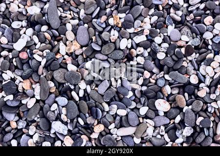 Hintergrund aus Kieselsteinen, Blick von oben. Die Textur von Meeressteinen. Grau-lila, weiße, gelbe Steine auf dem Meer. Natürliche Materialien und Farben aus Stein. Stockfoto