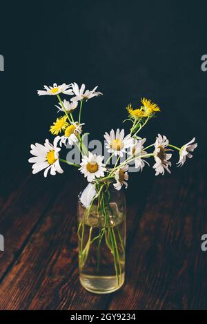 Kleiner Strauß wilder Kamillenblumen in Glasvase auf Holztisch Stockfoto