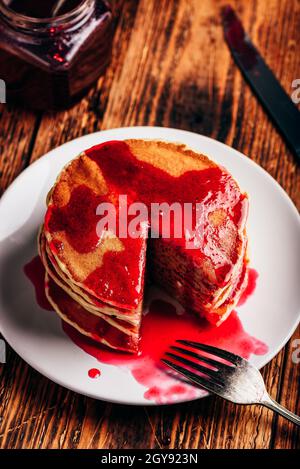 Stapel von amerikanischen Pfannkuchen mit roten Beeren Marmelade auf der Platte über rustikale Oberfläche Stockfoto