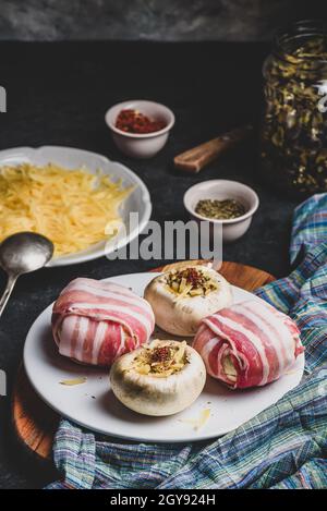 Zubereitung von mit Speck umwickelten Champignons, gefüllt mit geriebenem Cheddar-Käse Und Gewürzen Stockfoto