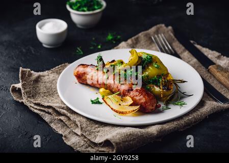 Schweinewurst gebacken mit grünen Paprika, Zwiebeln und Kräutern auf weißem Teller Stockfoto