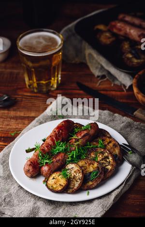 Gebackene Schweinswürste mit Auberginen und Lauch auf weißem Teller Garniert mit frischen Kräutern Stockfoto