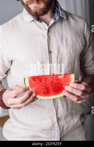 Bärtiger Mann im Leinenhemd hält in seinen Händen eine Scheibe reifer roter Wassermelone Stockfoto