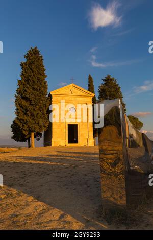 Alte Kirche von Vitaleta mit Bäumen auf beiden Seiten & Abbracio di luce von Helidon Xhixha in San Quirico d'Orcia, in der Nähe von Pienza, Toskana, Italien im September Stockfoto