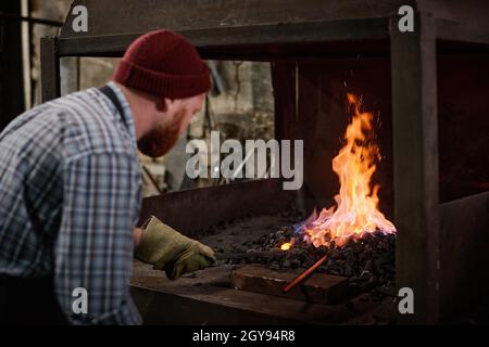 Arbeiter in Schutzhandschuhen, die Kohlen hinzufügen, um die Flamme im Ofen zu verbrennen Stockfoto