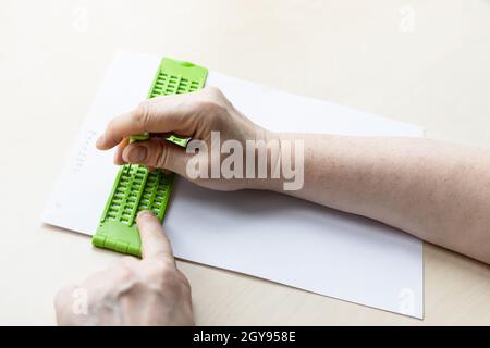 Weibliche Hand druckt Wörter in Braille mit Schiefer und Eingabestift aus der Nähe Stockfoto