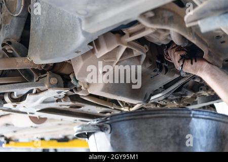 der automechaniker leitet altes Motoröl aus dem angehobenen Fahrzeug ab Stockfoto