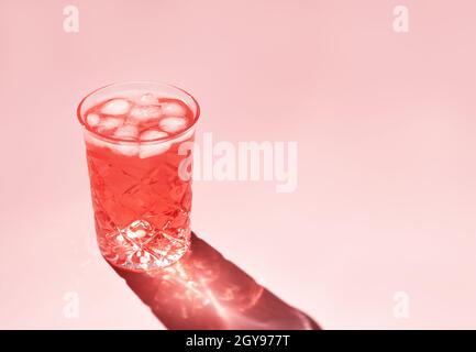 Schönes Kristallglas wirft langen Schatten vom Sonnenlicht auf rosa Hintergrund. Minimale kreative Komposition mit Kopierplatz. Sommergetränke-Konzept. Stockfoto