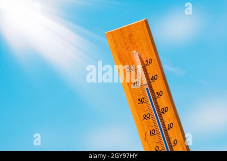 Thermometer mit einer Hochtemperaturanzeige auf einer Skala, vor einem Hintergrund von heller Sonne und einem blauen Himmel mit Wolken. Das Konzept der heißen, gefährlichen w Stockfoto