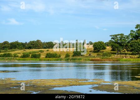 Blick auf die Felbrigg Hall in der Ferne über einen Teich, Bäume und Felder, Norfolk, England, fotografiert von einem öffentlichen Fußweg. Stockfoto