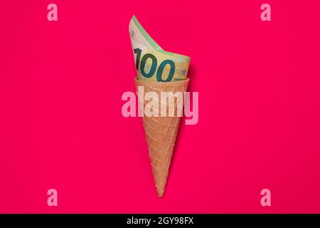 Eiscreme-Wafer-Konus mit zusammengerollter Euro-Papier-Banknote. Euro-Rechnung in Eis-Kegel gerollt Stockfoto
