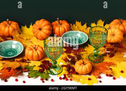 Mockup-grüne Vintage-Teller und -Becher, Ahornblätter, Kürbisse und Preiselbeeren auf weißer Tischdecke. Herbstkomposition mit Kopierraum. Halloween und Danksagekonzept. Stockfoto