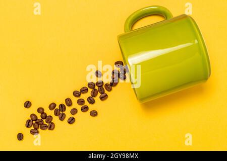 Verschüttete Kaffeebohnen aus der grünen Keramikschale auf dem Gelber Hintergrund Stockfoto