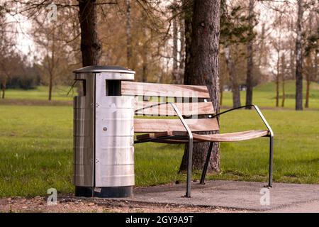 Holzbank und Metallabfallbehälter im Stadtpark. Moderner urbaner Stil an einem öffentlichen Ort. Stockfoto