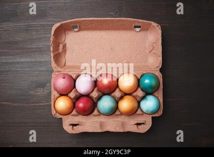 Verpackung mit farbigen Ostereiern auf Holztischhintergrund. Flach liegend. Stockfoto