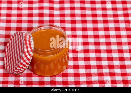 Selektive Konzentration auf ein Glas mit hausgemachter klassischer Sauce aus frischem Paprika mit Tomaten, Knoblauch und Basilikum auf einer rot karierten Tischdecke. Vorlage für f Stockfoto