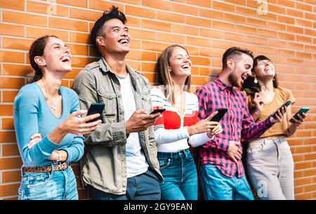 Multikulturelle Freunde lachen mit dem Smartphone an der Wand des Universitätscampus - Junge Menschen, die von mobilen Smartphones süchtig sind Stockfoto