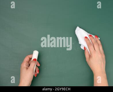Hand hält ein Stück weiße Kreide auf dem Hintergrund einer leeren grünen Kreidetafel, Präsentationskonzept, zurück zur Schule Stockfoto