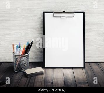 Leeres Büromaterial für Unternehmen. Klemmbrett mit leerem weißen Blatt Papier, Getränkehalter mit Stiften und Stiften, Visitenkarten. Stockfoto