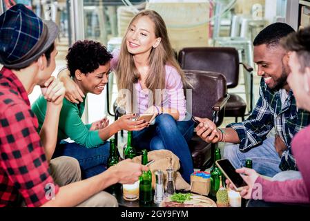 Freunde aus verschiedenen Rassen trinken Bier und haben Spaß mit Telefonen im Cocktailbar Restaurant - Freundschaftskonzept mit Menschen, die Zeit zusammen genießen Stockfoto