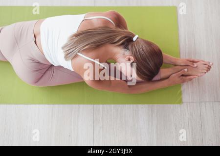 Das Sportmädchen, das den Trainer streckt, sitzt auf dem Garn. Toip-Ansicht Stockfoto