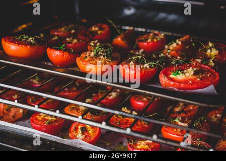 Halbierte Tomaten mit Kräutern und Knoblauch auf Backblech vorbereiten Im Ofen zum Konservieren Stockfoto