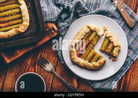 Mini-Galette mit Rhabarber-Scheiben auf weißem Teller und schwarzer Tasse Kaffee. Blick von oben Stockfoto