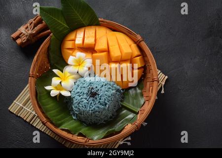 Mango und klebriger Reis, süßes thailändisches Dessert, gefärbt mit Schmetterlingsblüten auf dunklem Hintergrund Stockfoto