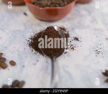 Löffel Kaffee und Tontöpfe mit gerösteten Kaffeebohnen auf weißer Marmoroberfläche Stockfoto