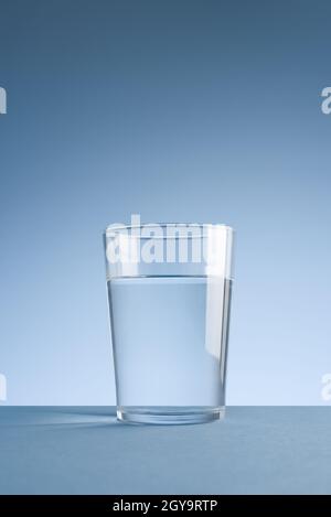 Minimalistisches Foto eines Glases sauberen Trinkwassers auf blauem Hintergrund, mit Copyspace Stockfoto