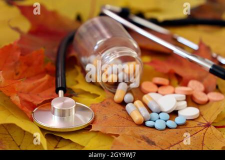 Stethoskop und verschiedene Pillen auf herbstlichen Ahornblättern. Konzept der Gesundheitsversorgung, Medikamente und Vitamine Stockfoto