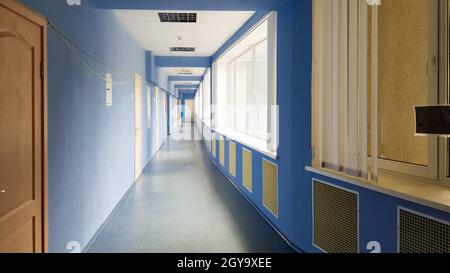 Ukraine, Kiew - 24. September 2019: Langer leerer Korridor ohne Menschen in einem Krankenhaus mit blauen Wänden, Holztüren und Fenstern. Sonnenstrahlen vom Wind Stockfoto