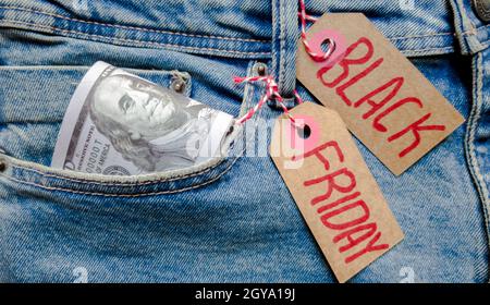 Gelddollar in viel Jeans-Tasche und Karton-Tag mit Text schwarz freitag. Blauer Hintergrund, Urlaubskonzept. Schwarzer Freitag - Internationaler Tag von Stockfoto