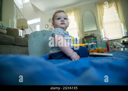 Kleiner Junge mit klobigen Armen, der allein auf dem Boden des Wohnzimmers sitzt. Stockfoto