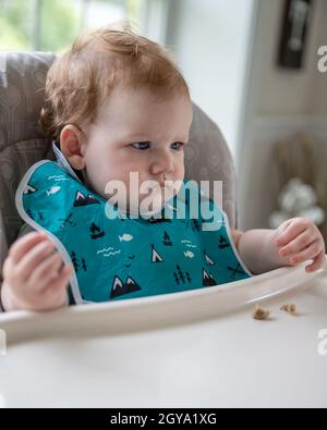 Kleiner Junge, der auf einem Hochstuhl sitzt und auf Essen wartet. Stockfoto
