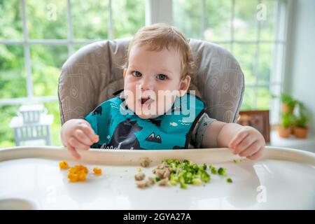 Baby Junge macht lustige Gesicht beim Essen mit seinen Händen. Stockfoto