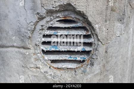 Lüftungsloch in Beton. Runder Lüftungsdeckel aus Metall für die Industrie. Rostiger und schmutziger alter runder Lüftungsrahmen mit horizontalen Metallstreifen Stockfoto