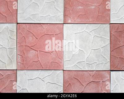 Betonüberzug aus grauen und roten Farben. Bürgersteig aus grauen und rosa Pflastersteinen aus der Nähe. Struktur, Hintergrund aus gelockert grau-orange Stein. Draufsicht auf den Stockfoto