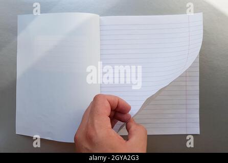 Designkonzept - Draufsicht einer hochwertigen männlichen Hand, die durch ein Blatt blau gestreiftes Notizbuch blättert. Draufsicht, Kopierbereich, flach liegend. Stockfoto