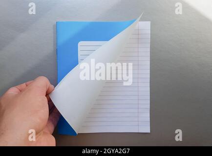 Designkonzept - Draufsicht einer hochwertigen männlichen Hand, die durch ein Blatt blau gestreiftes Notizbuch blättert. Draufsicht, Kopierbereich, flach liegend. Stockfoto