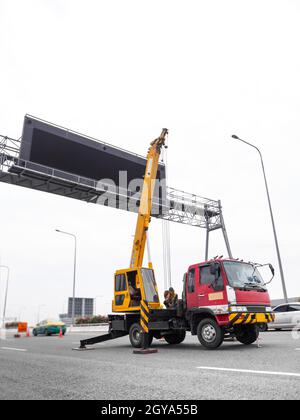 Baustellenkran hebt ein LED-Schild Blank Plakatwand Auf blauem Himmel Hintergrund für neue Werbung Stockfoto