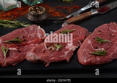 Aus dem Tenderloin auf Holzschneidebrett schneiden sich drei Stücke traditionelles dünnes Steak mit Olivenöl, Salz, Rosmarin und Pfeffer. Raw Black Angus Prim Stockfoto