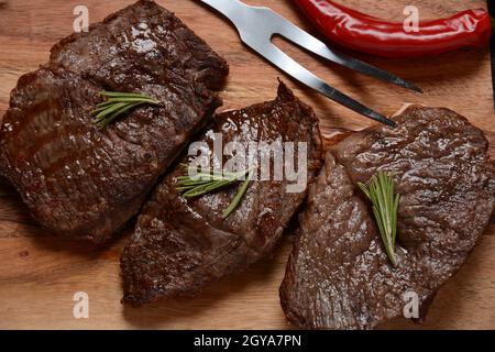 Gegrilltes saftiges Rindersteak mit Rosmarin, gebratenes Fleisch, Nahaufnahme. Top Blade Steaks auf Holzbrett Stockfoto