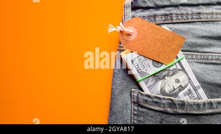 Viele Hunderte von Dollar Banknoten in einer Jeans-Tasche in einer Geldbörse mit einem Karton-Tag, Preisschild. Geldbörse und Dollar in Jeans-Tasche. Platz kopieren, platzieren Stockfoto