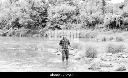 Zufriedener Fischer. Angeln erfordert, dass Sie achtsam und vollständig im Moment anwesend sein. Brutal Mann tragen Gummistiefel stehen im Flusswasser. Fisher maskulin Stockfoto