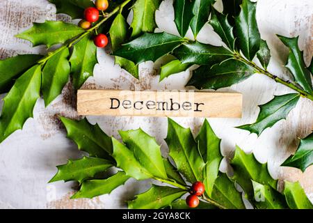 Holzblock mit Dezember-Wort auf weißem Holzhintergrund mit Stechpalme verziert Stockfoto