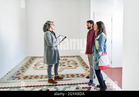 Immobilienmakler, der multirassischen Männern und Frauen Daten zeigt, während sie in einer Mietwohnung stehen Stockfoto
