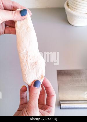 Die Hände der Frau strecken ein Stück Teig, um die Qualität des Mehls zu überprüfen Stockfoto
