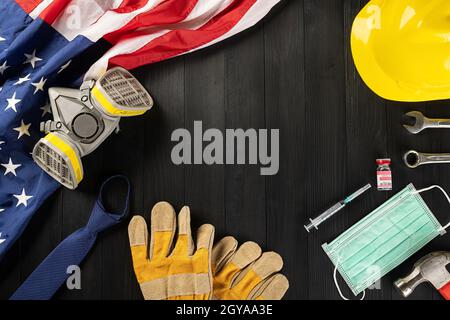 Happy Labor Day beim Ausbruch des Coronavirus. Mehrere Konstrukteur Arbeitswerkzeuge, Labor COVID-19 Impfstoff, medizinische Gesichtsmaske schützende und amerikanische Flagge wi Stockfoto